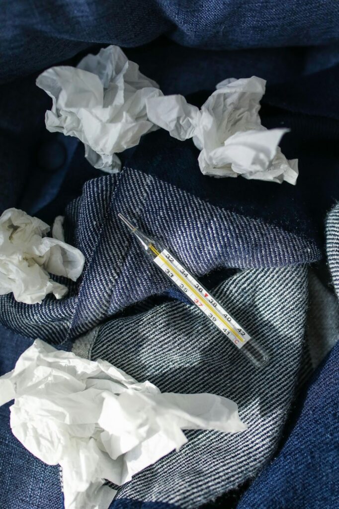 Picture of a glass mercury-style thermometer resting on a blue striped cloth surrounded by crumpled white tissues.
