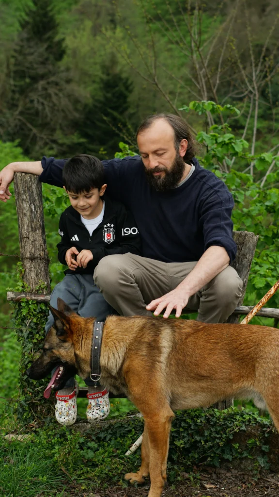 Picture of a man and a young boy sitting on a rustic wooden fence next to a German Shepherd