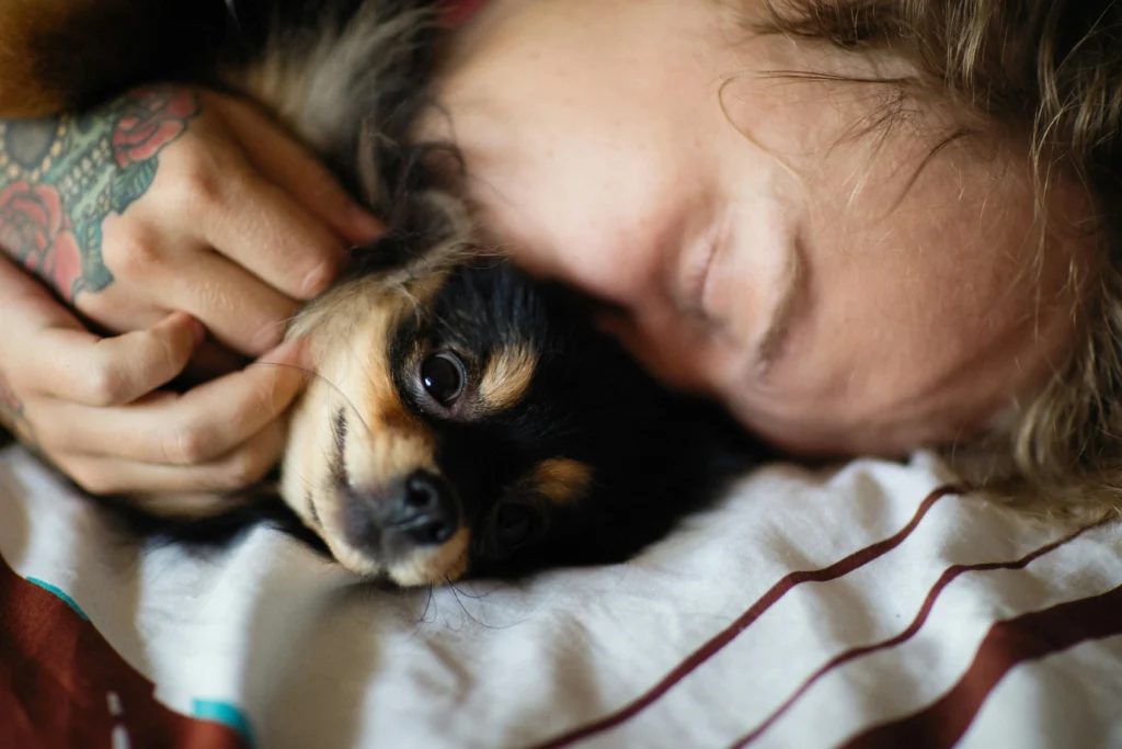 picture of a person sleeping face to face with a small black and tan long haired dog on a striped pillow