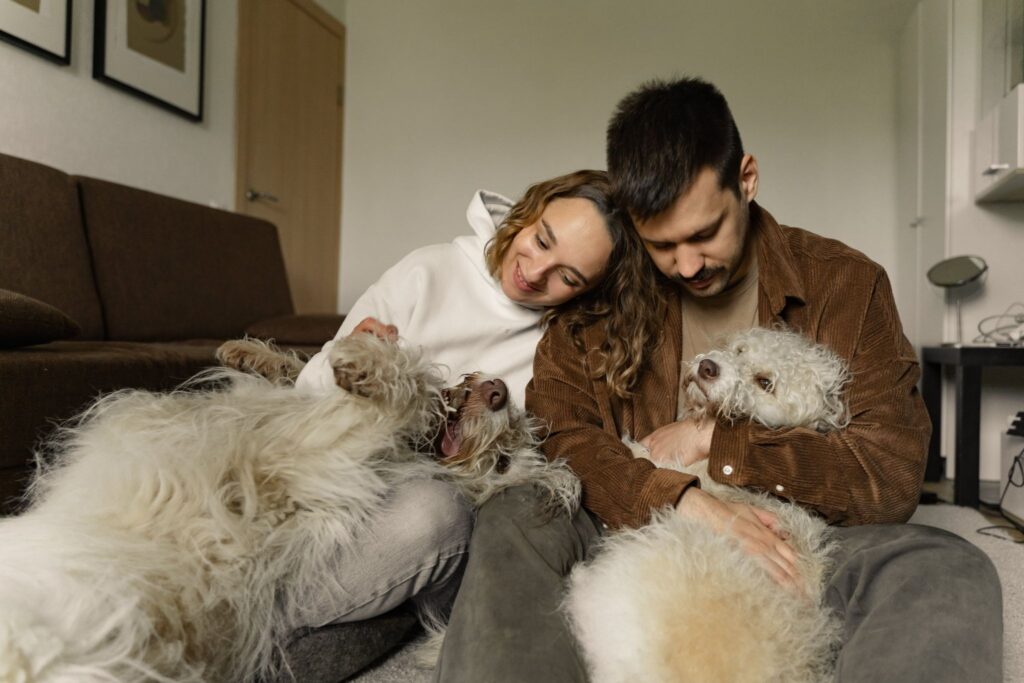 Picture of a man and woman relaxing on the floor with two fluffy dogs.